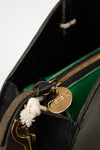 Close-up of a 'Clare V.' gold tag on a black leather handbag.