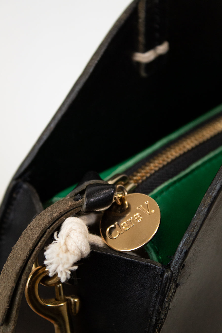 Close-up of a 'Clare V.' gold tag on a black leather handbag.