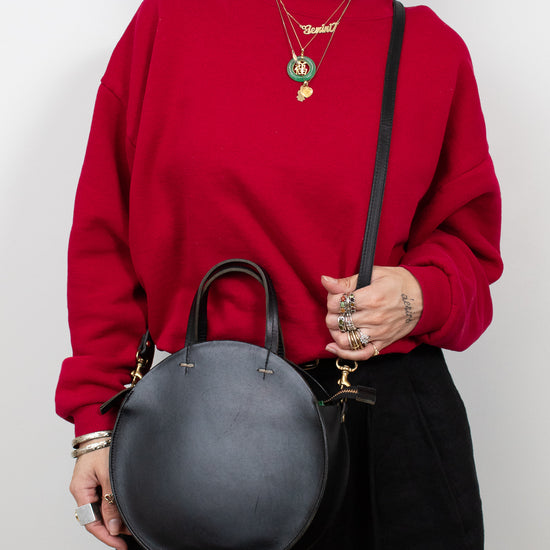 Person wearing a red sweater holding a black handbag against a white background