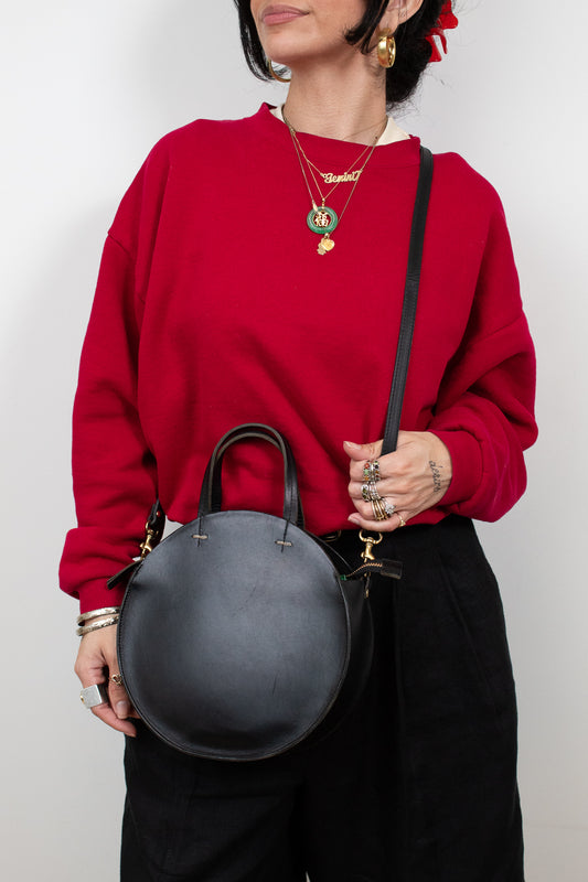 Person wearing a red sweater holding a black handbag against a white background
