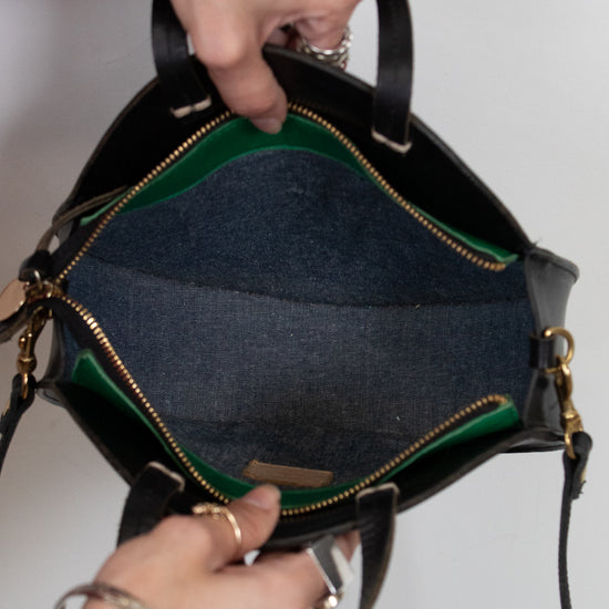 Person holding a black handbag open with green details against a plain background