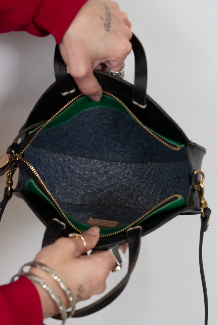 Person holding a black handbag open with green details against a plain background