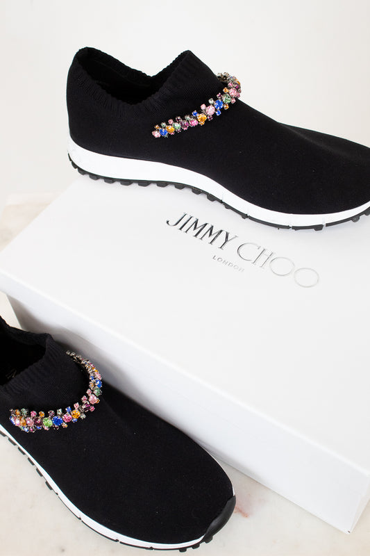 Black slip-on shoes with colorful embellishments on a white box with 'Jimmy Choo' branding.