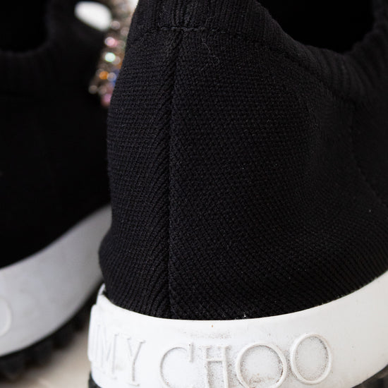 Black sneaker with white sole featuring 'Jimmy Choo' branding on a marble surface.