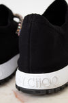 Black sneaker with white sole featuring 'Jimmy Choo' branding on a marble surface.