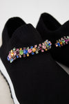 Black slip-on shoes with colorful gemstone embellishments on a light gray background