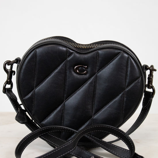 Black quilted heart-shaped handbag with a brand logo on a white background