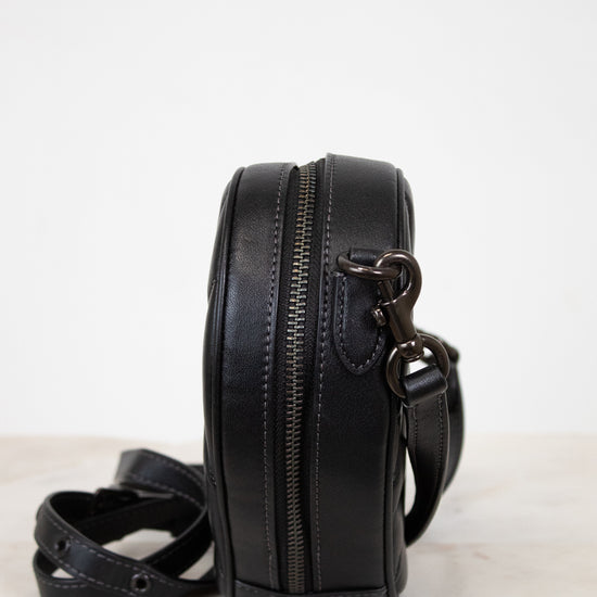 Black leather crossbody bag with a strap on a white surface