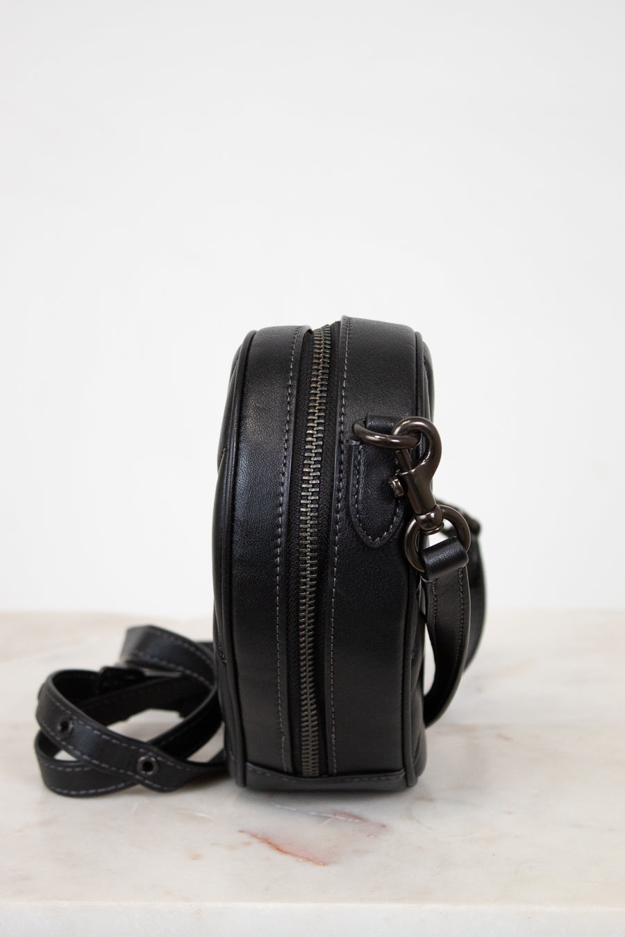 Black leather crossbody bag with a strap on a white surface