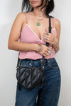 Person wearing a pink checkered top, blue jeans, and holding a black quilted handbag against a plain background.
