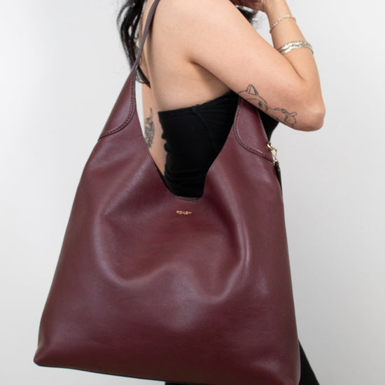 Person wearing a large burgundy leather bag against a plain background