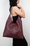 Person wearing a large burgundy leather bag against a plain background