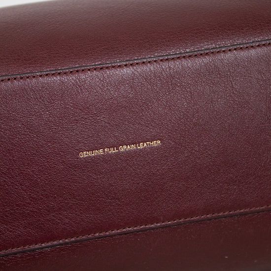 Close-up of a maroon leather bag with 'Genuine Full Grain Leather' text on a marble surface.