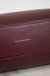 Close-up of a maroon leather bag with 'Genuine Full Grain Leather' text on a marble surface.