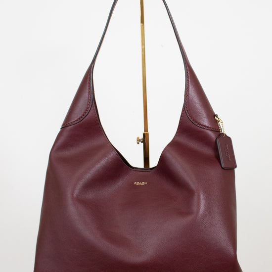 Maroon handbag with gold zipper on a white background