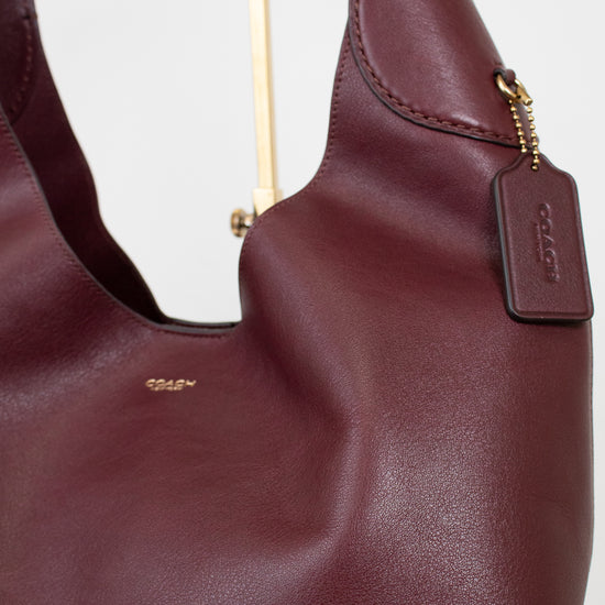 Maroon handbag with gold Coach logo on a white background
