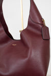 Maroon handbag with gold Coach logo on a white background