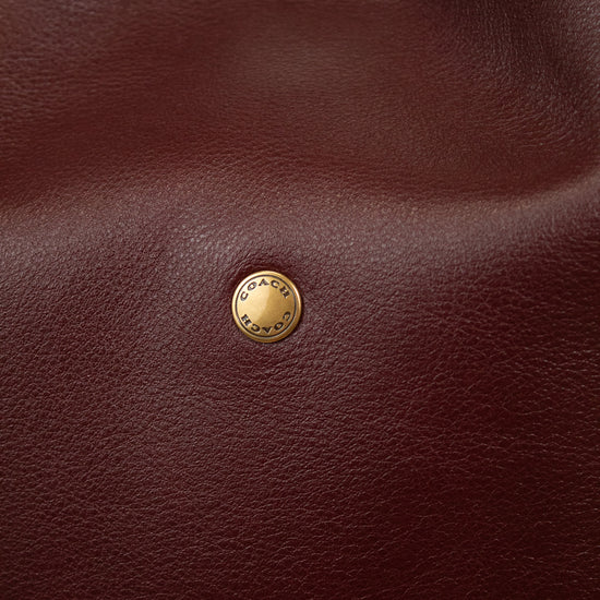 Close-up of a maroon leather bag with a gold logo emblem.