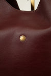 Close-up of a maroon leather bag with a gold logo emblem.