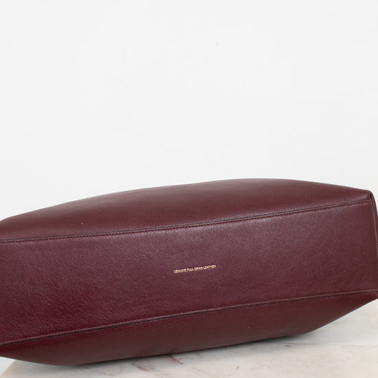 Maroon leather bag on a light marble surface with a white background