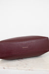 Maroon leather bag on a light marble surface with a white background