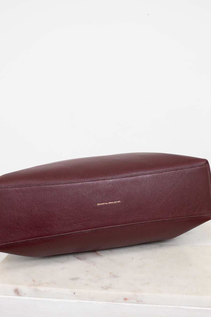 Maroon leather bag on a light marble surface with a white background