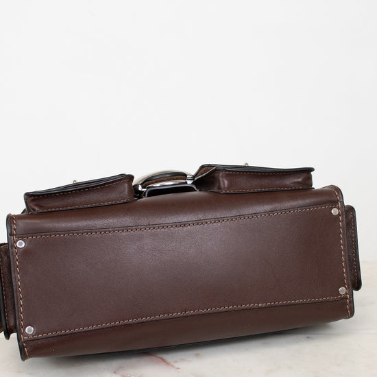 A dark brown leather tool pouch or organizer with silver metal rivets and a silver buckle, resting on a light marble surface against a white background.