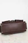 A dark brown leather tool pouch or organizer with silver metal rivets and a silver buckle, resting on a light marble surface against a white background.
