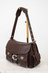 A dark brown leather shoulder bag with silver-tone hardware, displayed on a gold-colored stand against a white background.