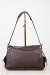 A dark brown leather shoulder bag with a front pocket and gold-tone hardware, displayed on a stand against a white background.