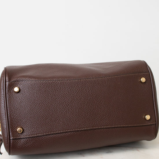 A brown pebbled leather handbag shown from the bottom, resting on a white marble surface against a white background.