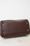 A brown pebbled leather handbag shown from the bottom, resting on a white marble surface against a white background.