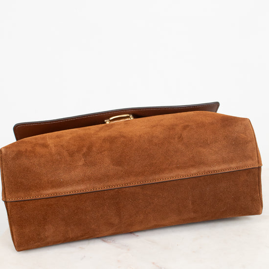 A brown suede clutch bag with a gold-tone metal clasp, resting on a white marble surface against a white background.