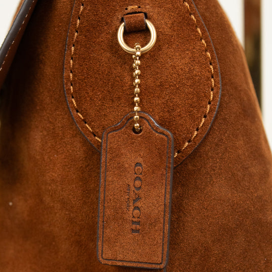 Close-up of a brown suede handbag with a gold-tone ring and chain holding a brown leather Coach hangtag.