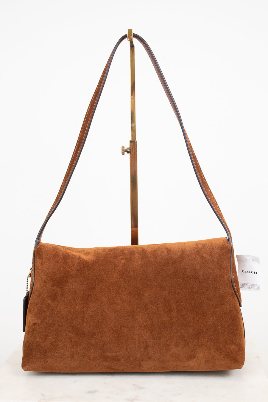 A brown suede shoulder bag with a long brown leather strap and a gold-tone metal stand, photographed against a clean white background.