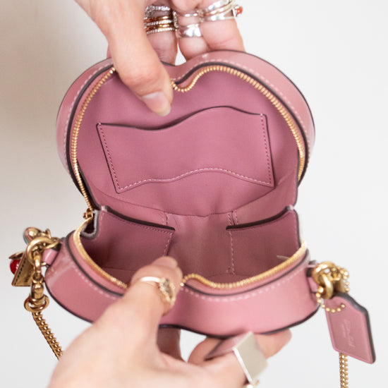 Pink heart-shaped bag with gold accents held open by a person against a neutral background