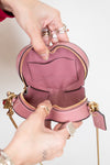 Pink heart-shaped bag with gold accents held open by a person against a neutral background