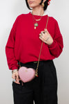 Person wearing a red sweater and holding a pink heart-shaped bag against a white background