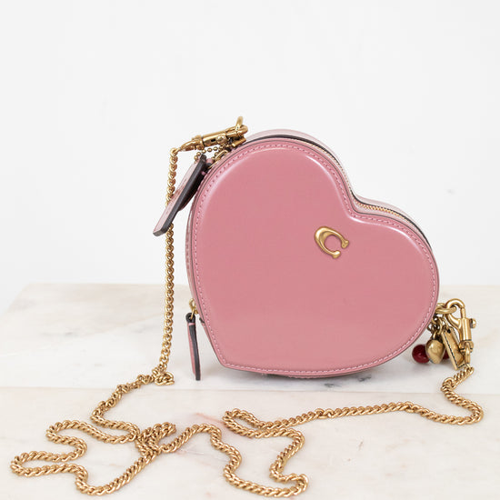 Pink heart-shaped handbag with gold chain on a white marble surface