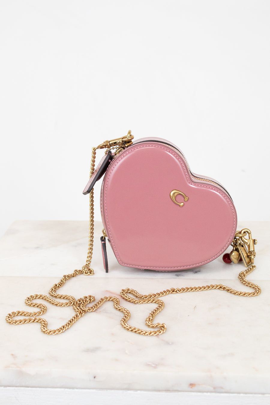 Pink heart-shaped handbag with gold chain on a white marble surface