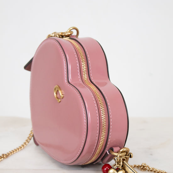 Pink handbag with gold chain and heart charm on a white background