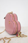Pink handbag with gold chain and heart charm on a white background