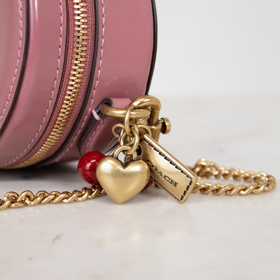 Pink round handbag with gold chain and heart-shaped charm on a light background