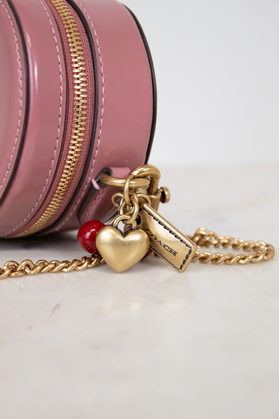 Pink round handbag with gold chain and heart-shaped charm on a light background