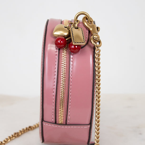Pink handbag with gold chain and red and gold charm details on a light background