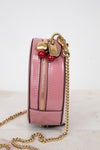 Pink handbag with gold chain and red and gold charm details on a light background