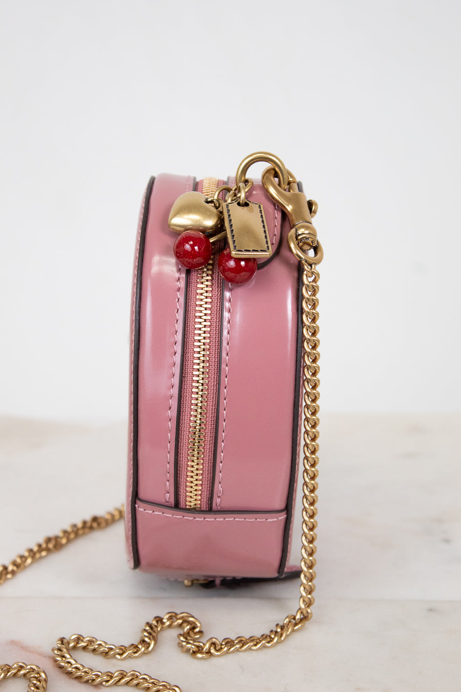 Pink handbag with gold chain and red and gold charm details on a light background