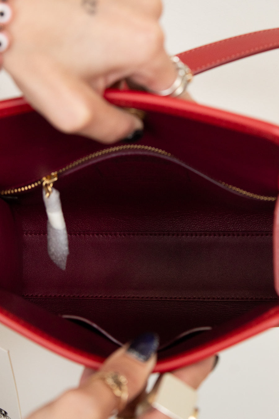 Red handbag with a gold zipper being held open, showing the interior.