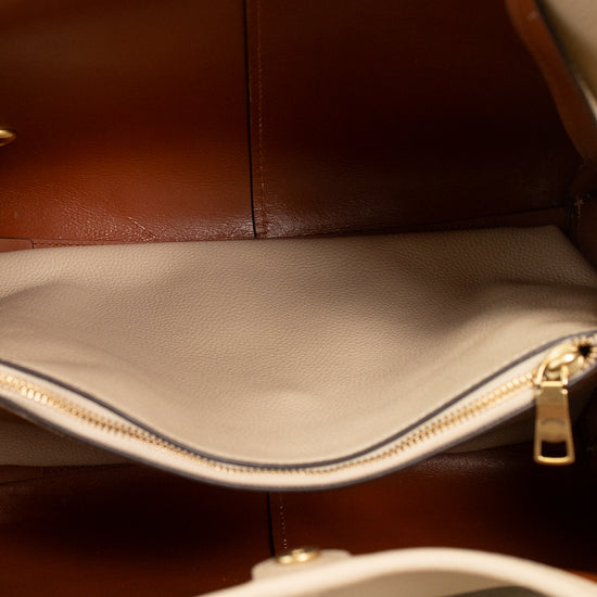 Close-up of the interior of a handbag, showing a brown and beige leather interior, a zippered compartment pocket, and a hand with red nail polish holding the bag open.