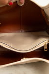 Close-up of the interior of a handbag, showing a brown and beige leather interior, a zippered compartment pocket, and a hand with red nail polish holding the bag open.